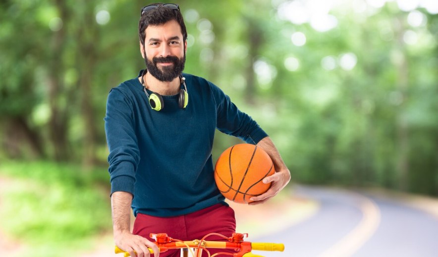 A man holding a basketball beside a bicycle on a tree-lined path